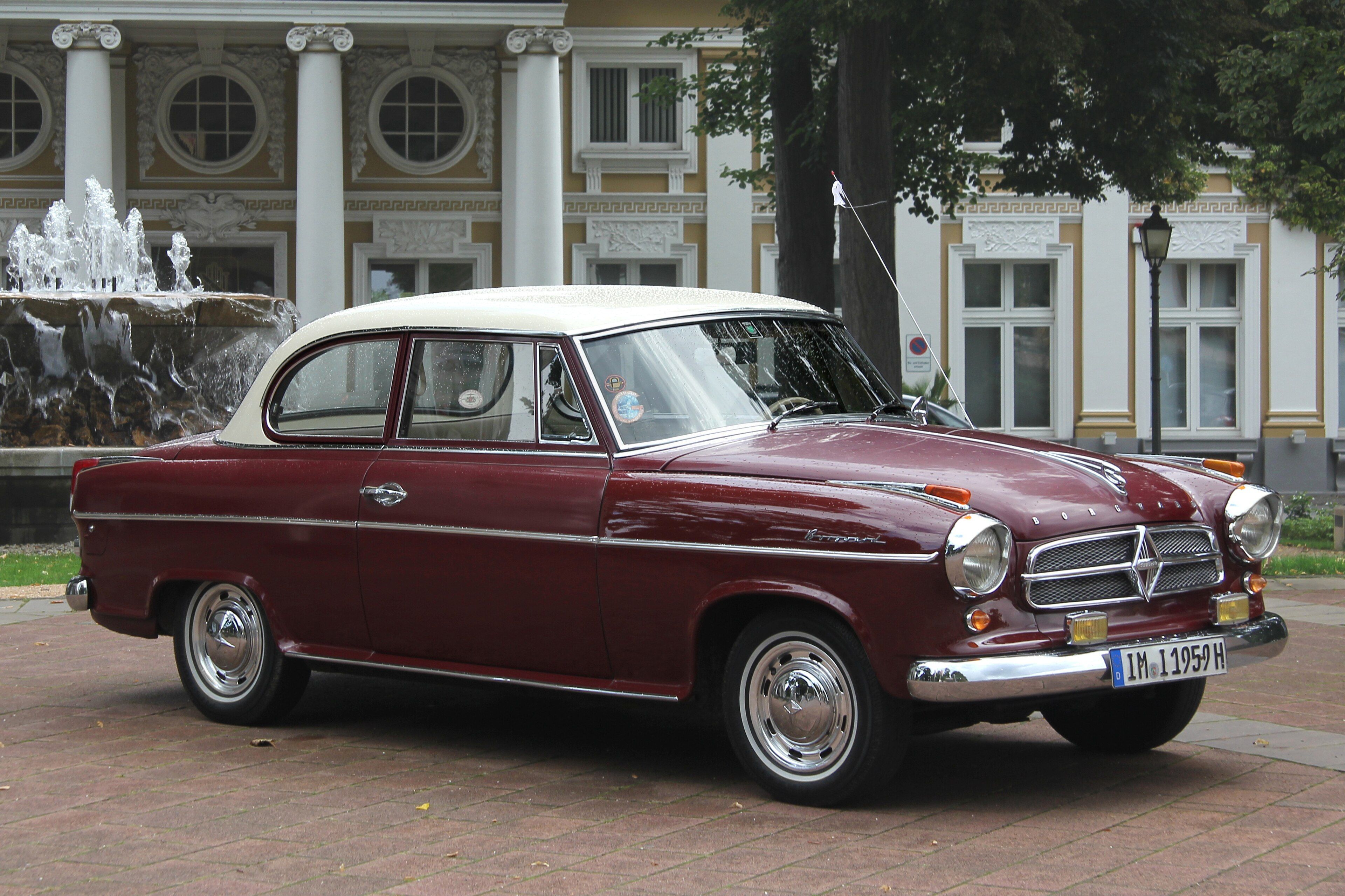 Maroon and cream 1959 Borgward Isabella coupé parked by a fountain, front three-quarter view