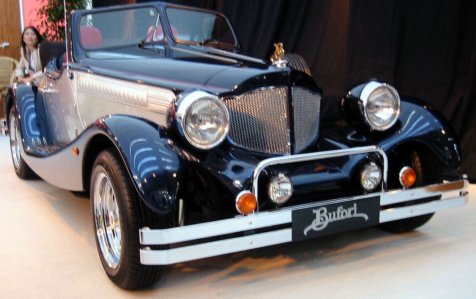 Dark blue Bufori MK II roadster, front three-quarter view, showing its 1930s-inspired long bonnet, cycle wings and mesh grille.