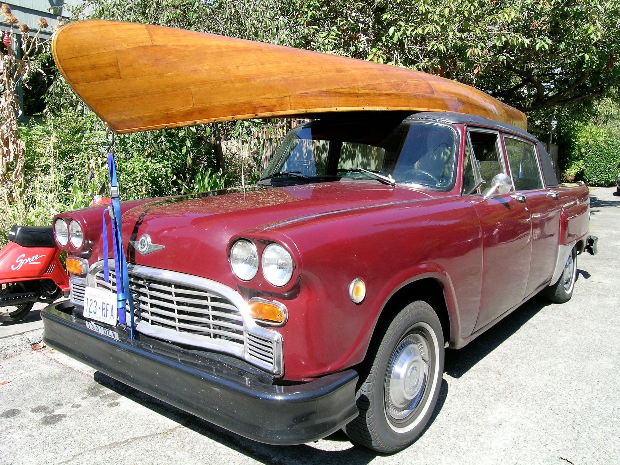 Maroon 1980 Checker Marathon sedan with a canoe on the roof, front three-quarter view