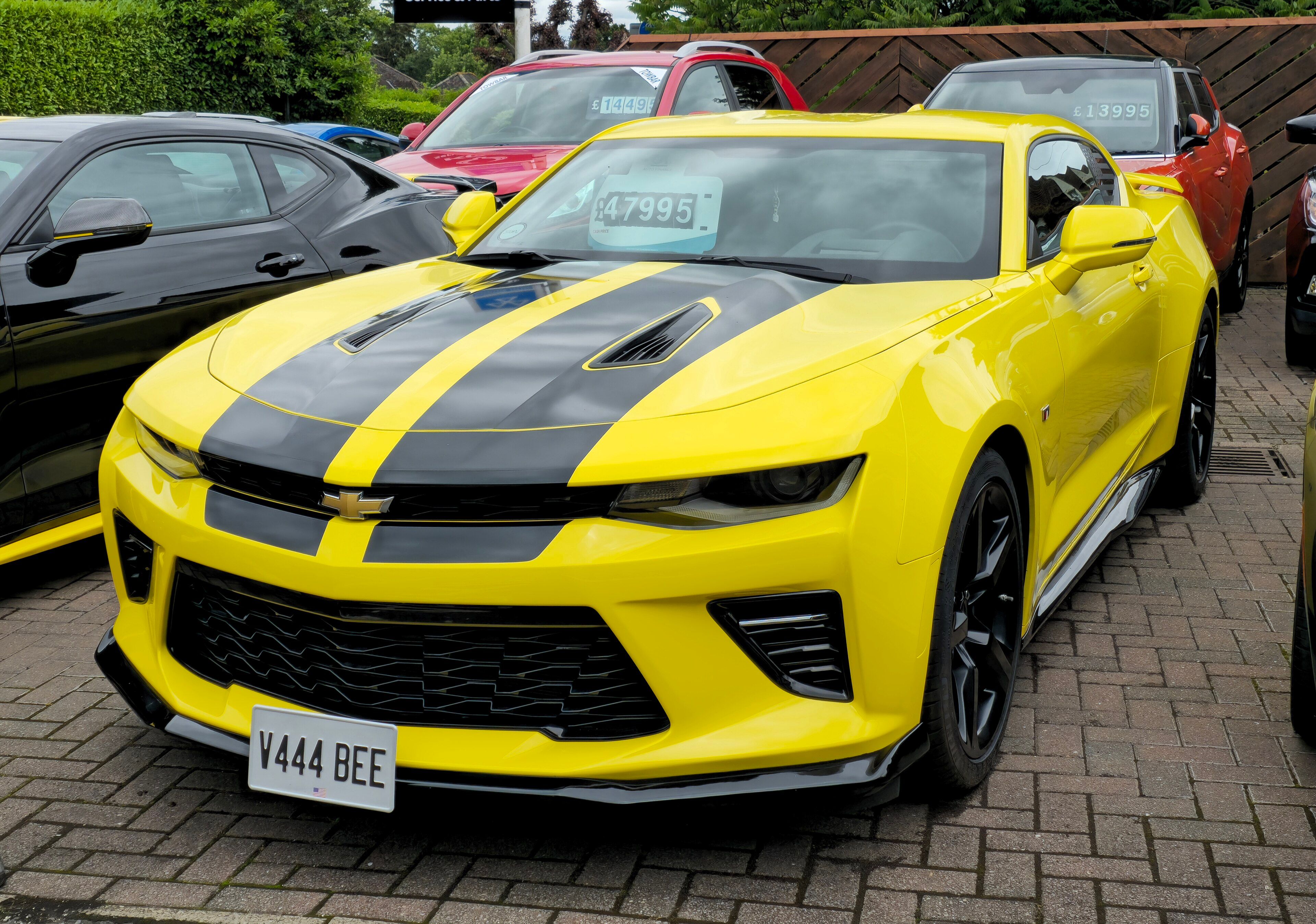 Yellow 2018 Chevrolet Camaro coupe with black racing stripes, front three-quarter view