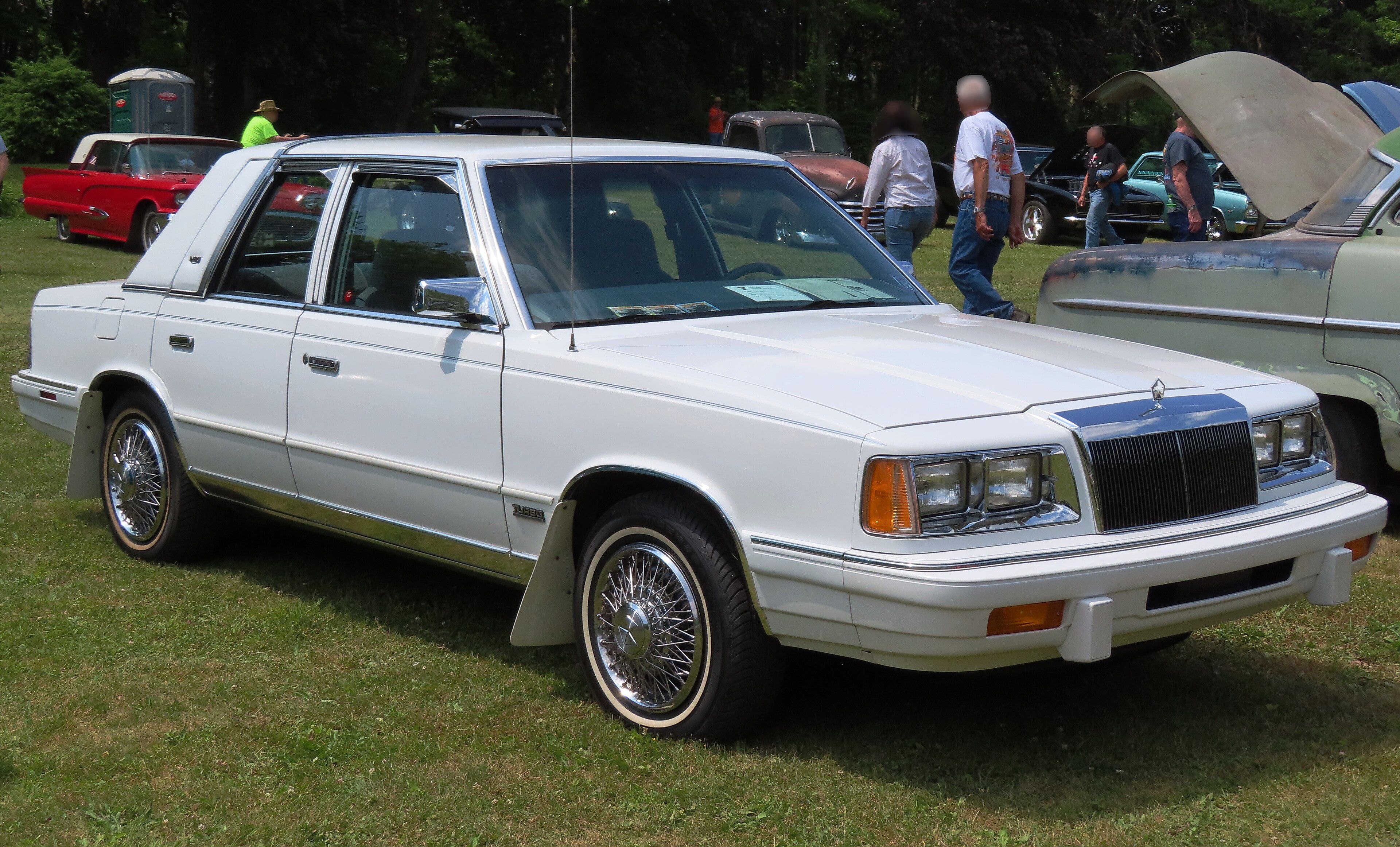 White 1988 Chrysler LeBaron four-door sedan at a car show, front three-quarter view