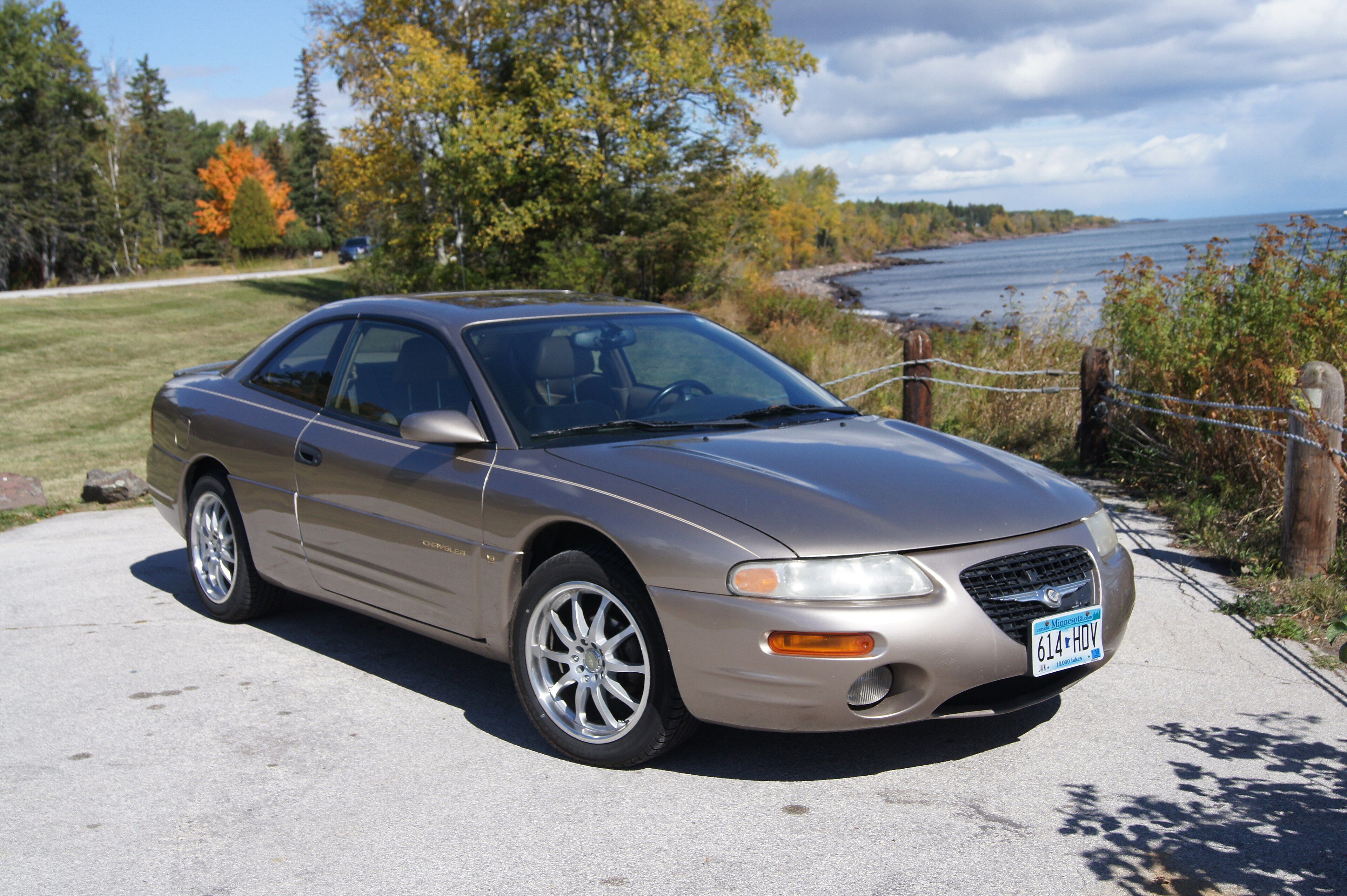 Gold 1999 Chrysler Sebring LXi coupe parked by a lakeshore, front three-quarter view