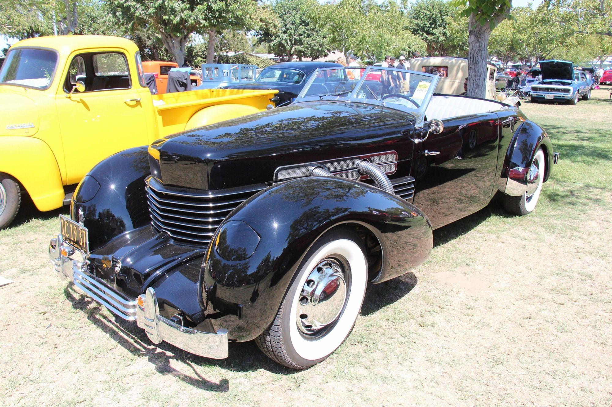 Black 1937 Cord 812 Supercharged Cabriolet, front three-quarter view with external chrome exhaust pipes exiting the hood