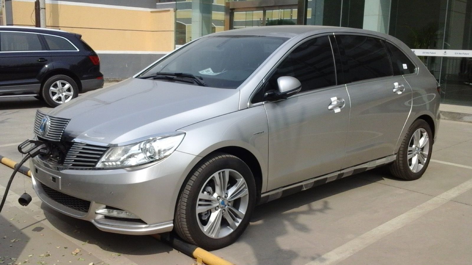 Silver Denza EV charging at a Chinese dealership, front three-quarter view