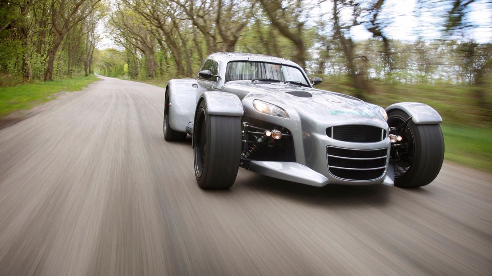 Silver Donkervoort D8 GT 270 travelling at speed on a tree-lined road, front three-quarter view