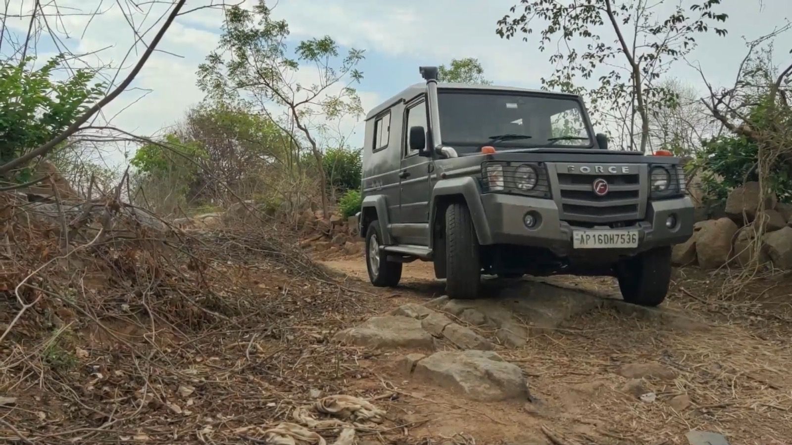 Grey three-door Force Gurkha off-roading on a rocky trail, front three-quarter view