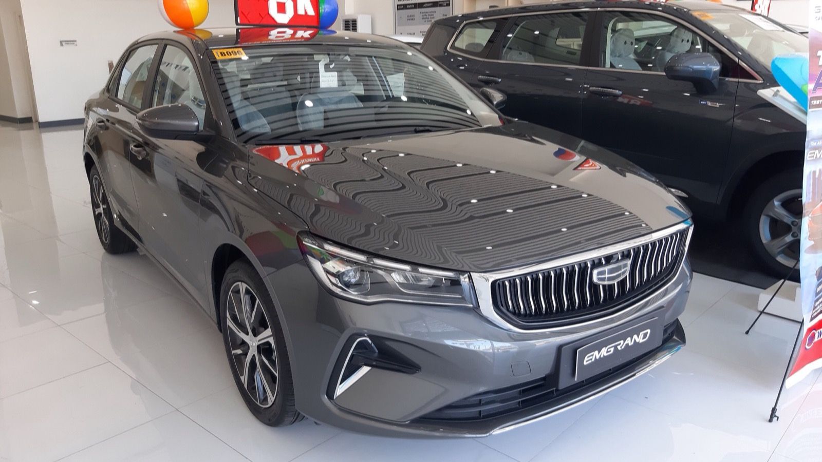 Grey 2024 Geely Emgrand 1.5 Comfort sedan in a dealership showroom, front three-quarter view
