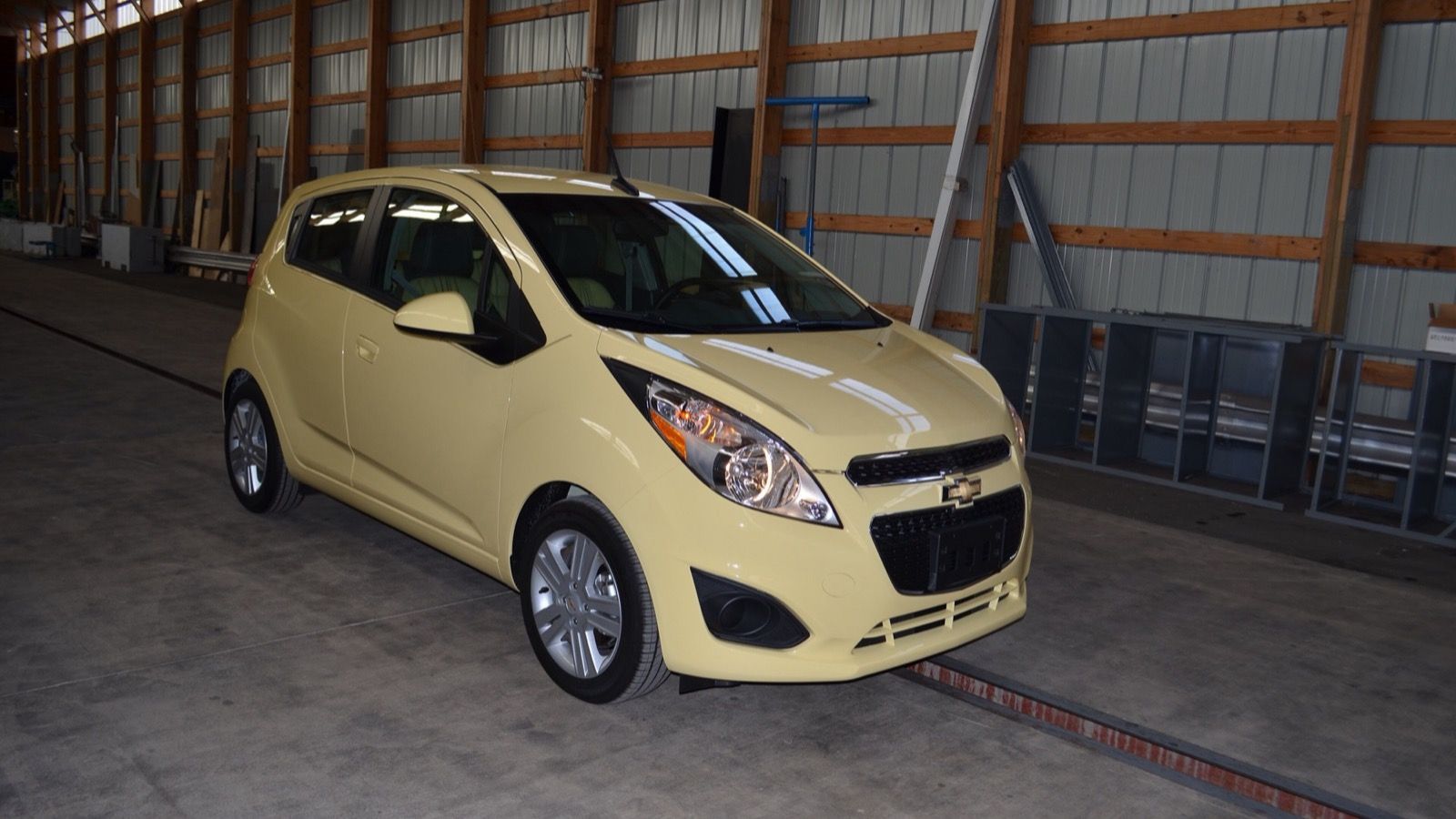 Pale-yellow 2014 Chevrolet Spark 1LS hatchback photographed before crash testing, front three-quarter view