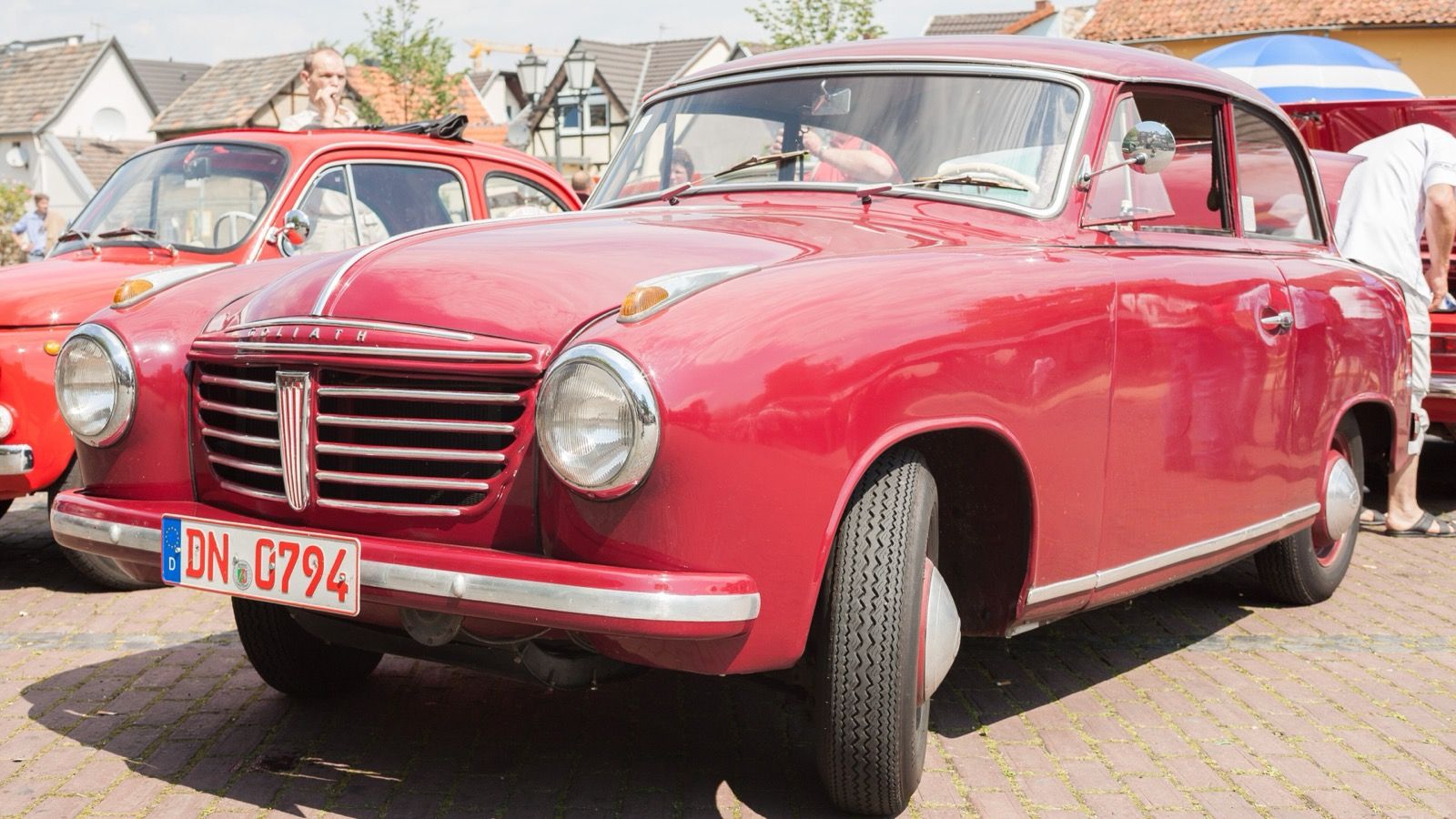 Red 1955 Goliath GP700 two-door saloon at an outdoor classic car meet, front three-quarter view