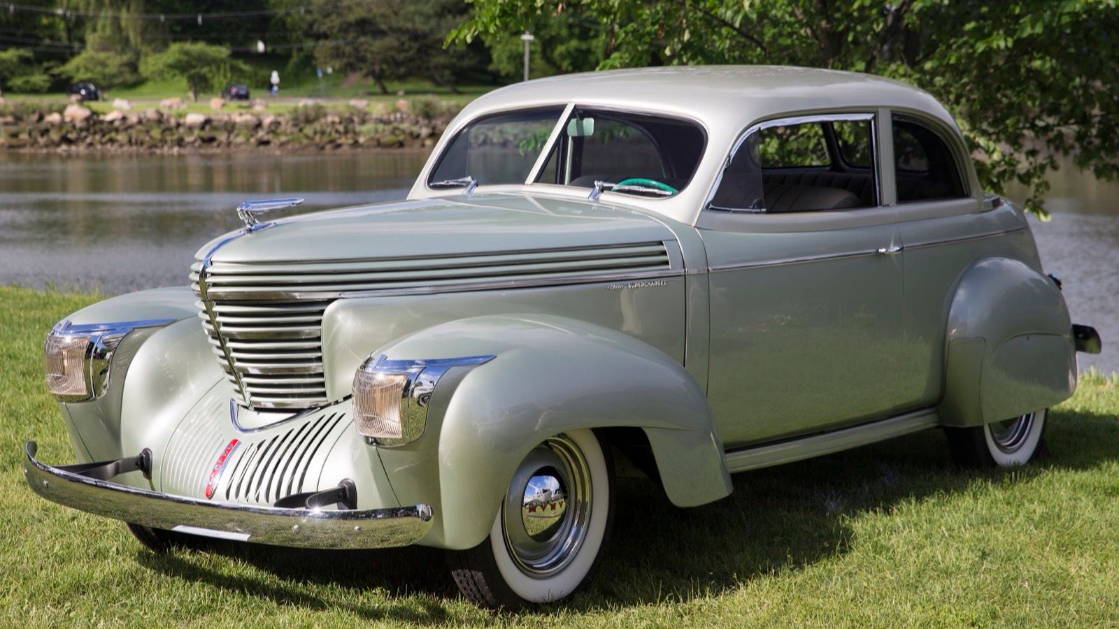 Pale green 1939 Graham supercharged Combination Coupe beside a lake, front three-quarter view