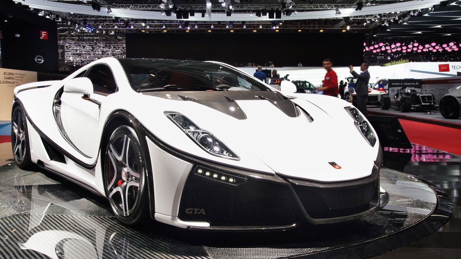 White second-generation GTA Spano with exposed carbon detailing on a turntable at the 2015 Geneva Motor Show, front three-quarter view