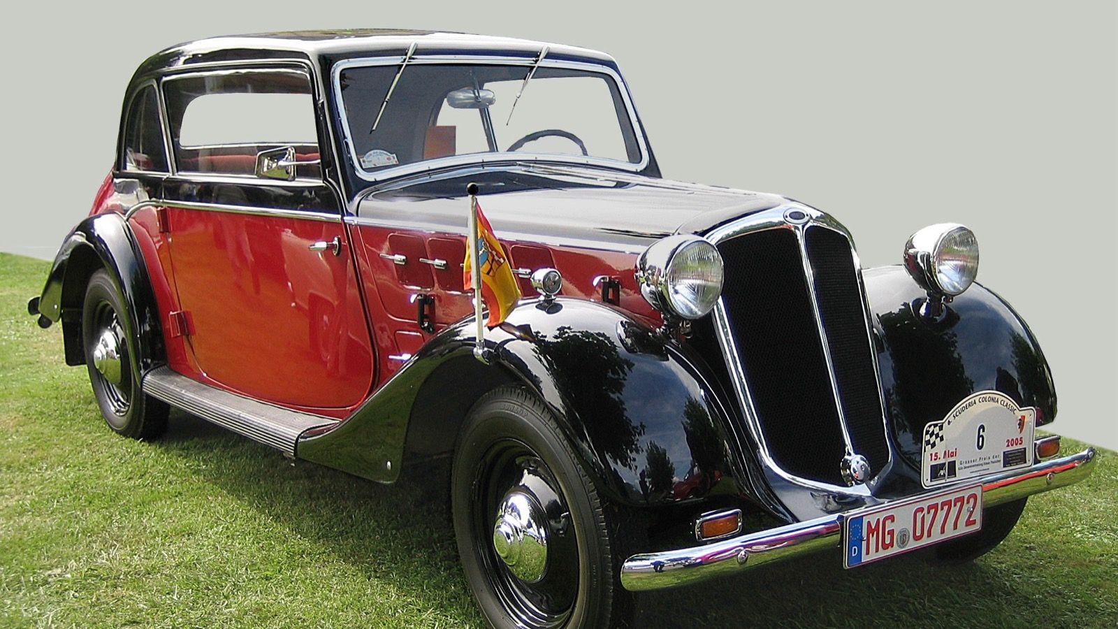 Red and black 1937 Hansa 1100 cabriolet displayed on grass at a classic-car event, front three-quarter view