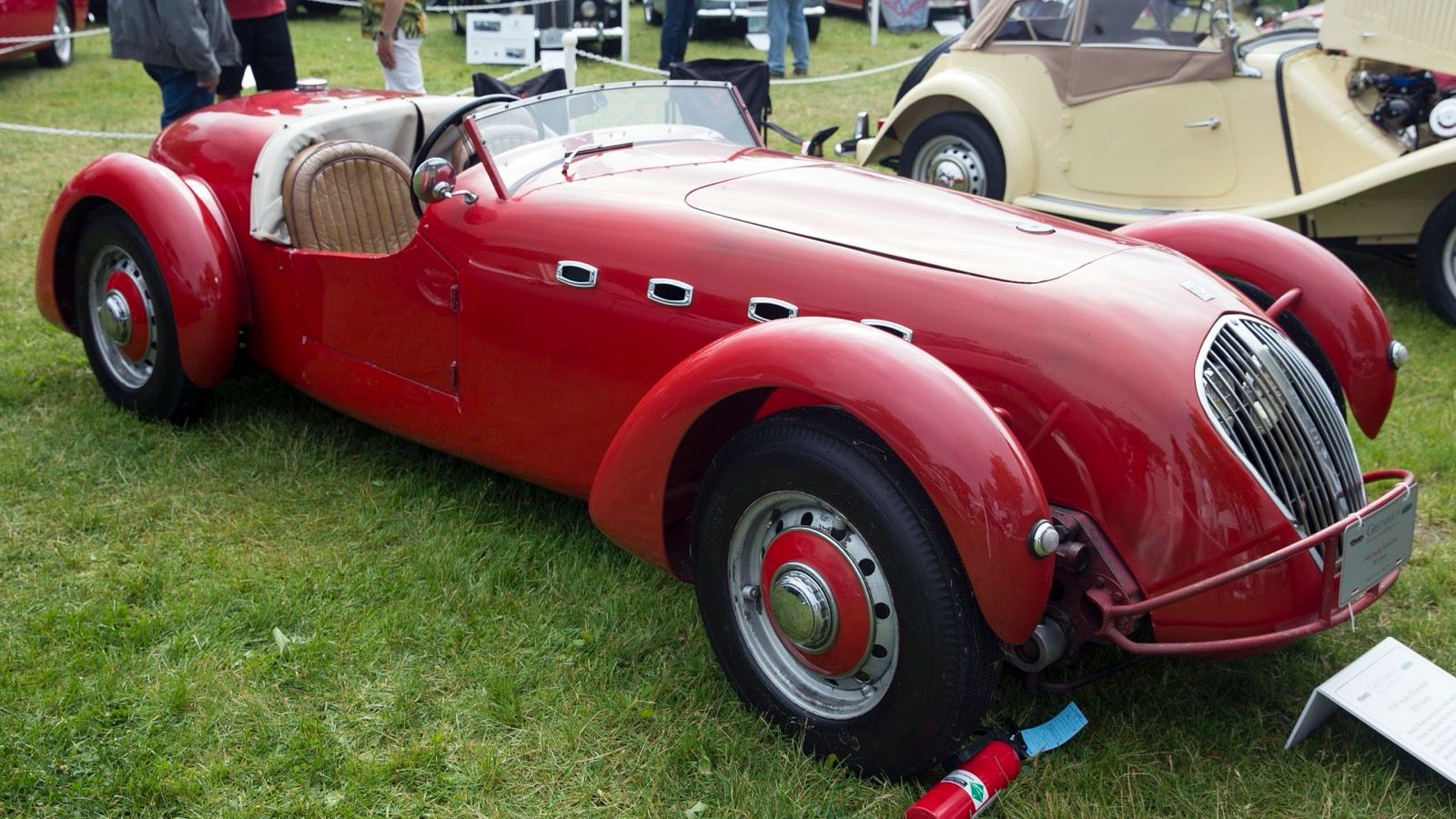 Red 1949 Healey Silverstone D-Type on grass at a concours, front three-quarter view