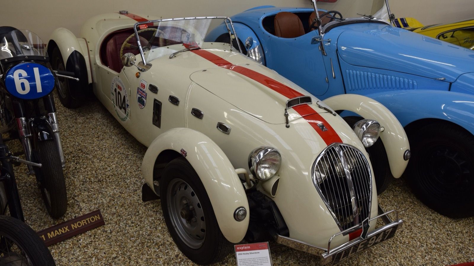 Cream 1950 Healey Silverstone D-Type with a red racing stripe on museum display, front three-quarter view