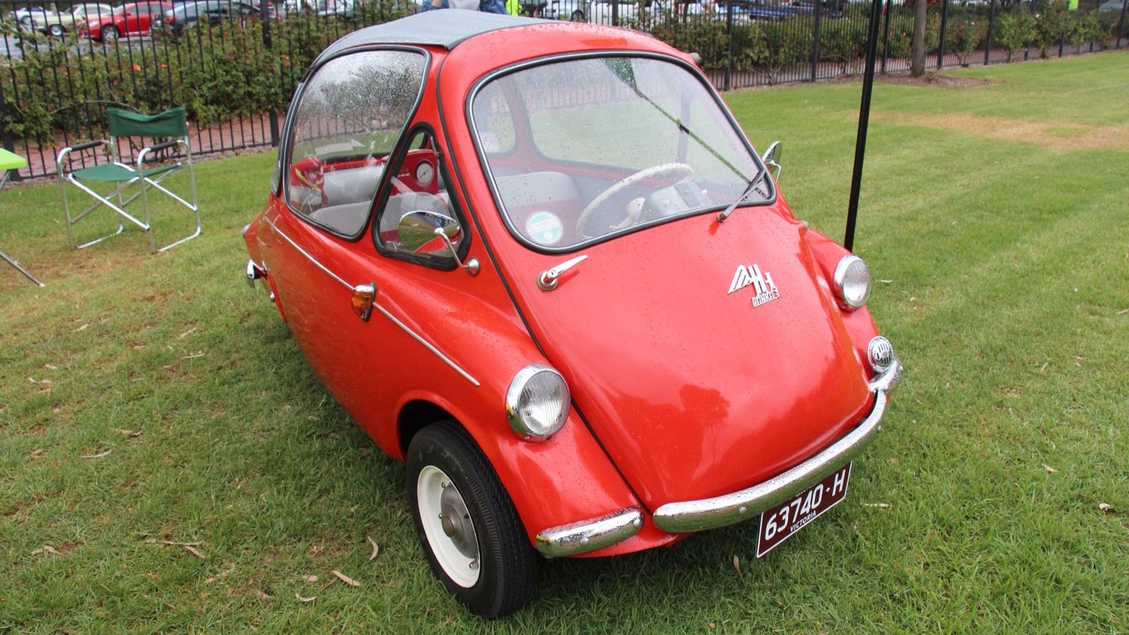 Red 1957 Heinkel Kabine 200 microcar on grass, front three-quarter view showing the front-hinged door and bubble canopy
