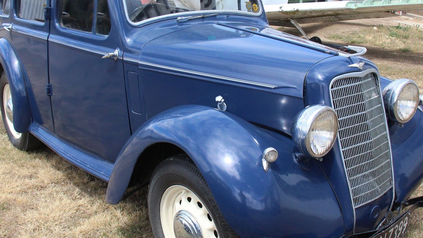 Blue 1936 Hillman Minx Magnificent saloon parked on grass beside a hangar, front three-quarter view