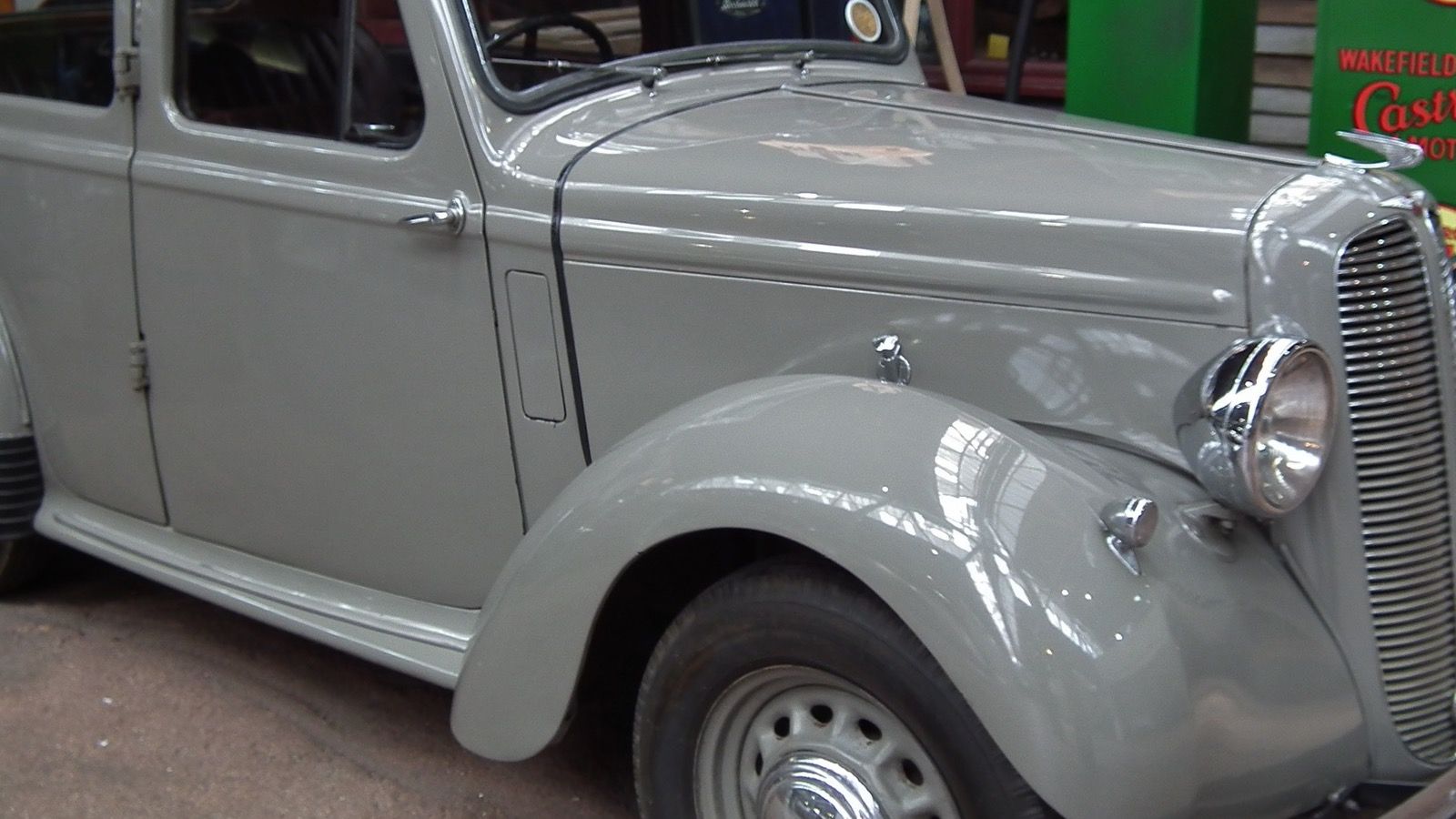 Grey 1938 Hillman Minx Magnificent saloon on museum display beside a period petrol pump, front three-quarter view