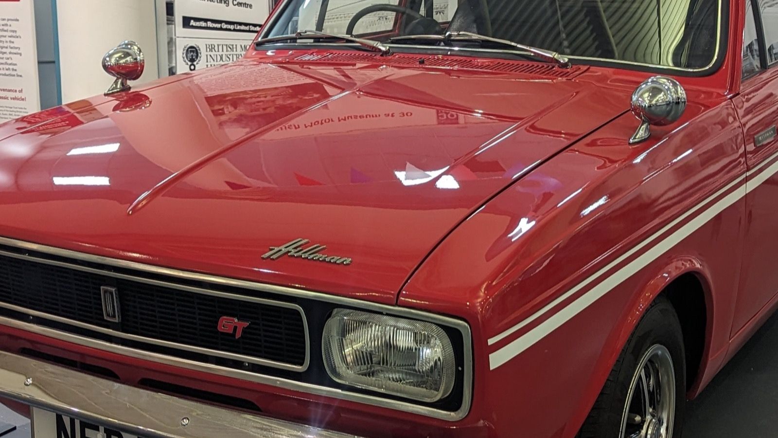 Red 1969 Hillman Minx GT with white side stripes on museum display, front three-quarter view