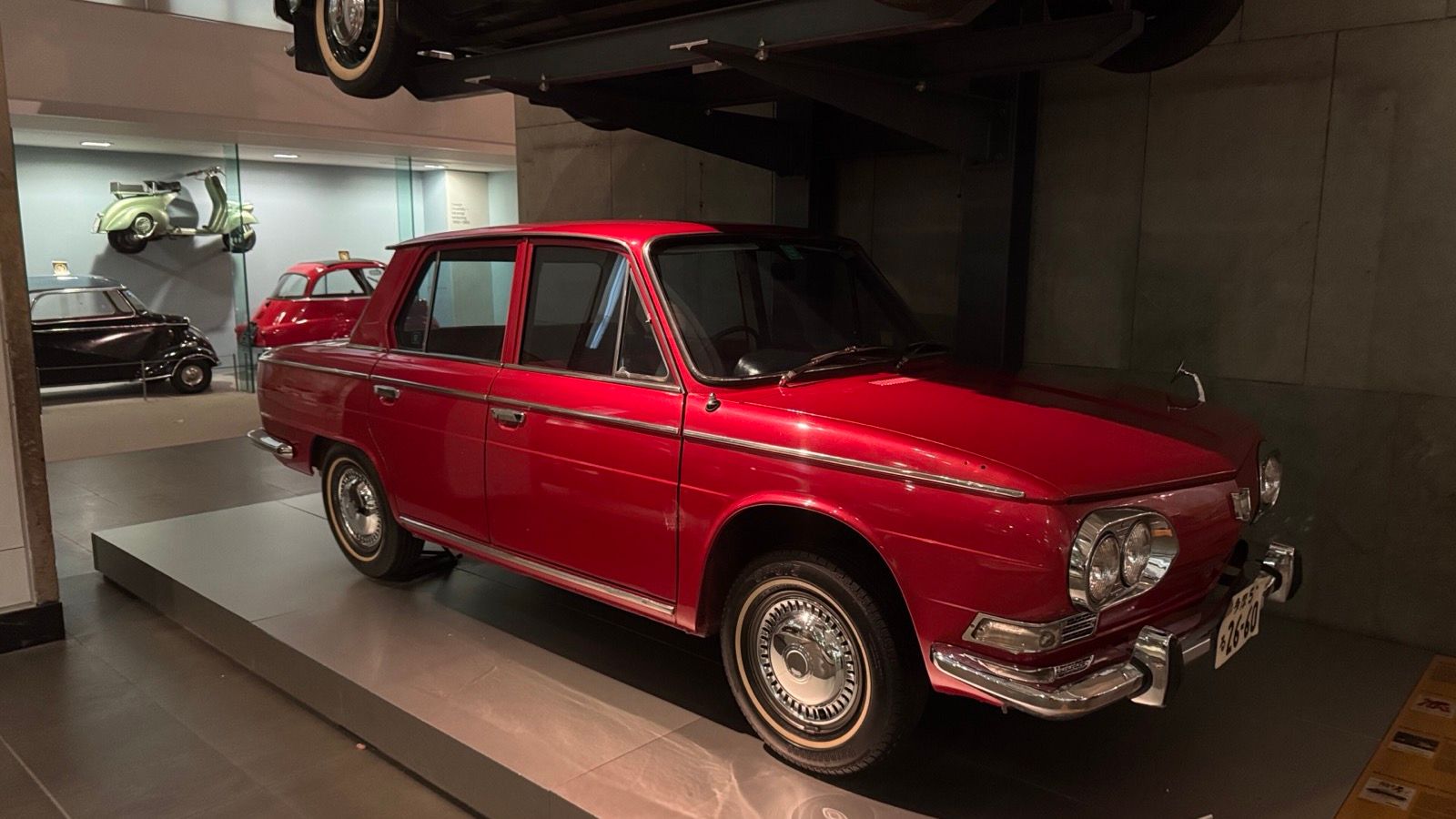Red 1965 Hino Contessa 1300 (PH10) four-door sedan on museum display, front three-quarter view