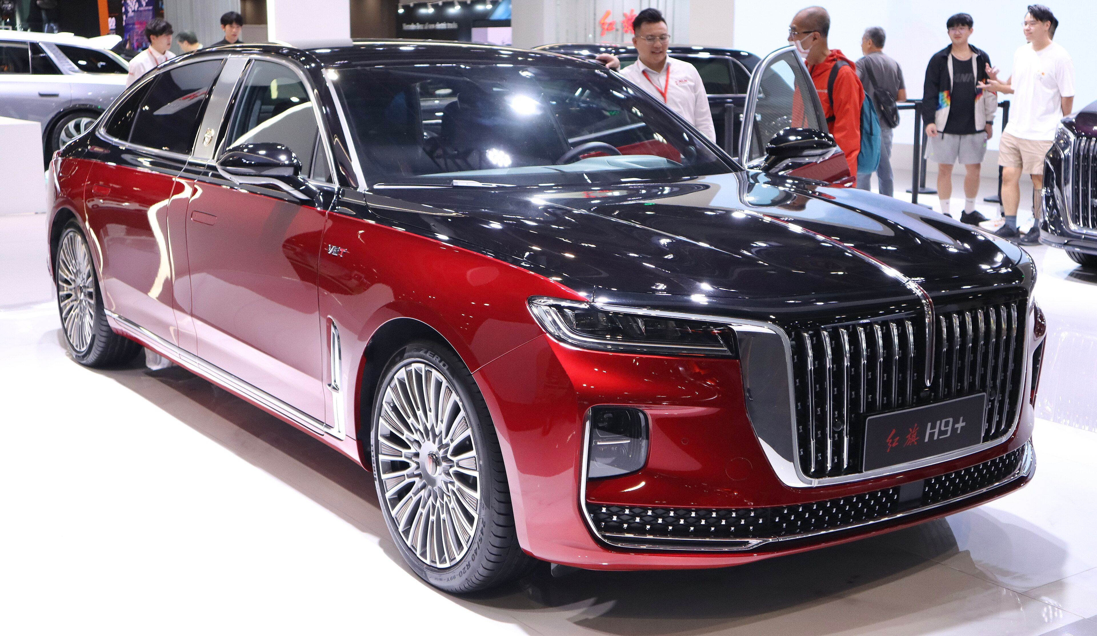 Two-tone red and black 2023 Hongqi H9+ long-wheelbase sedan on an auto-show stand, front three-quarter view.