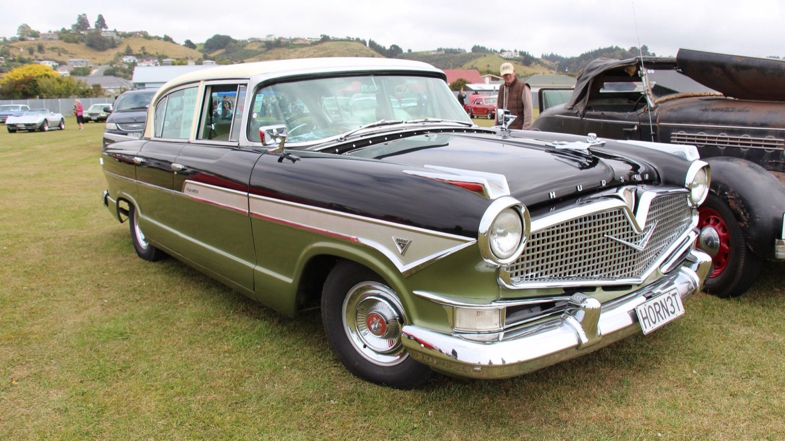 Black and olive green 1957 Hudson Hornet V8 four-door sedan on grass, front three-quarter view