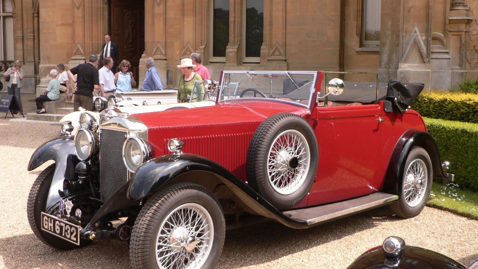 Red and black high-chassis Invicta 4½-litre drophead coupé, front three-quarter view on gravel outside a country house