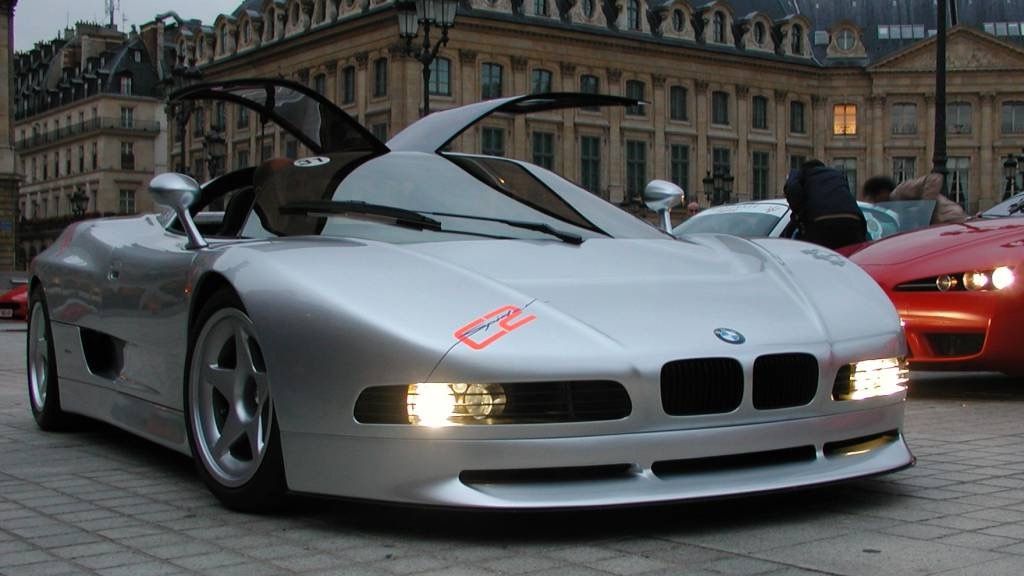 Silver BMW Nazca C2 with its canopy doors raised, parked in a Paris square, front three-quarter view