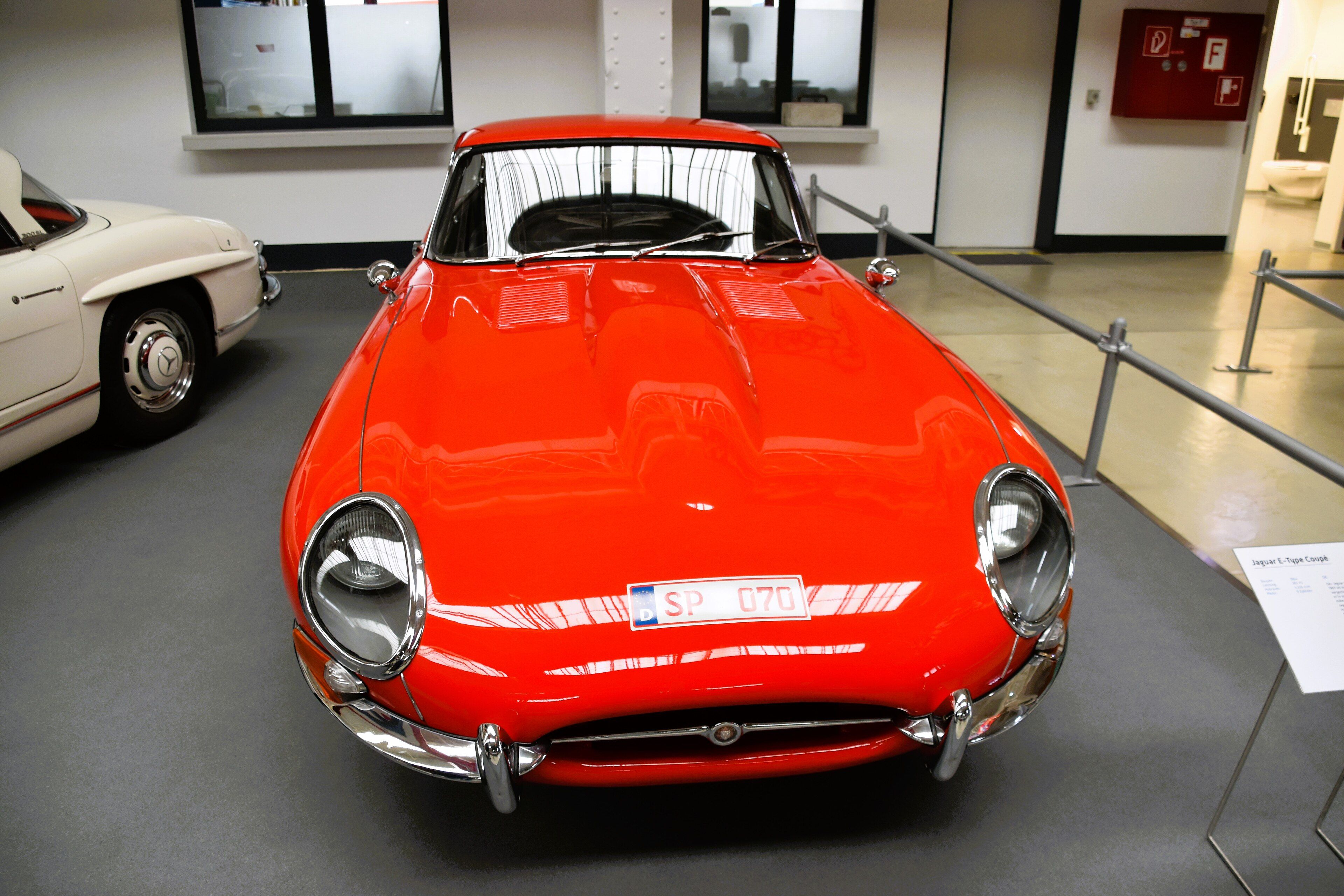 Red 1964 Jaguar E-Type 3.8 Series 1 fixed-head coupe on museum display, front view showing covered headlights