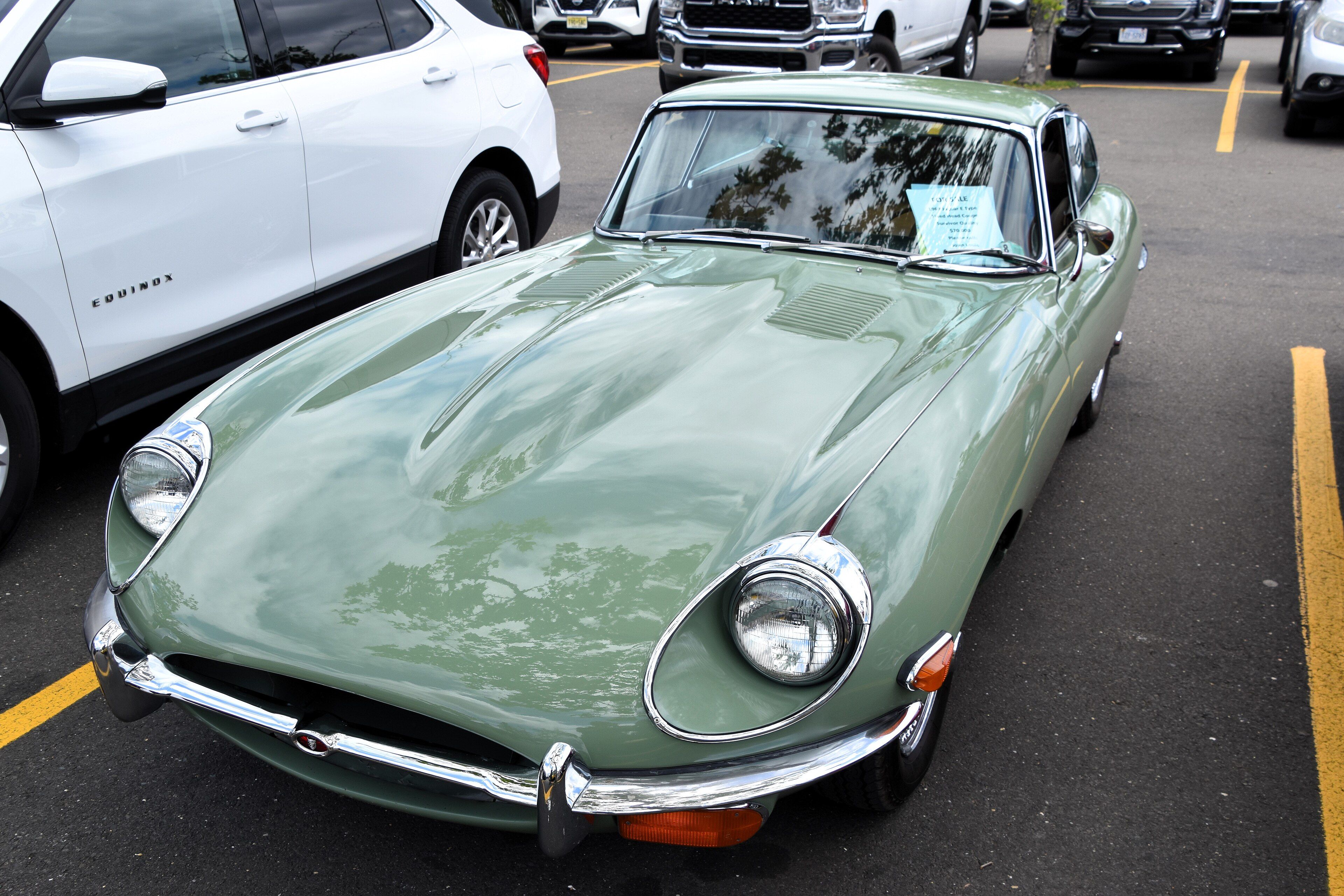 Pale green 1969 Jaguar E-Type 4.2 Series 2 coupe in a parking lot, front three-quarter view showing open headlights