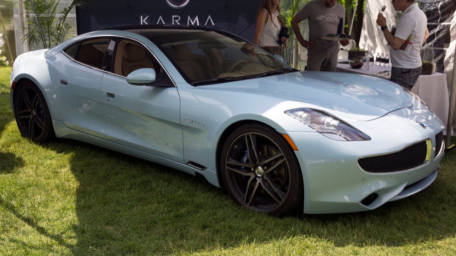 Light blue 2018 Karma Revero on grass at an outdoor event, front three-quarter view