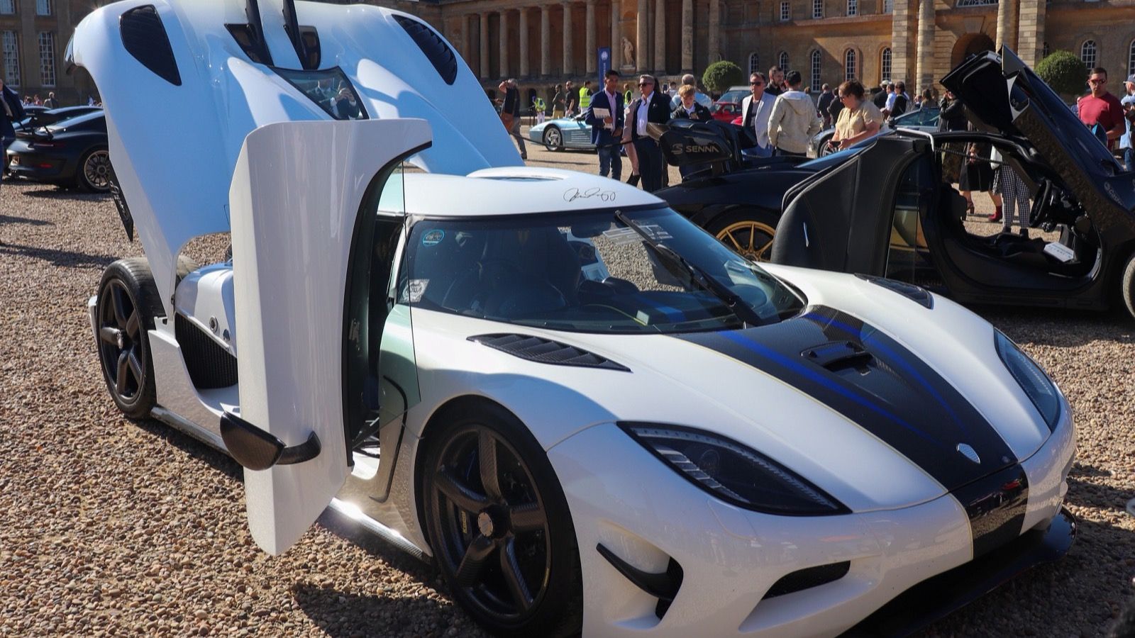 White 2011 Koenigsegg Agera with blue stripes and dihedral doors raised, front three-quarter view