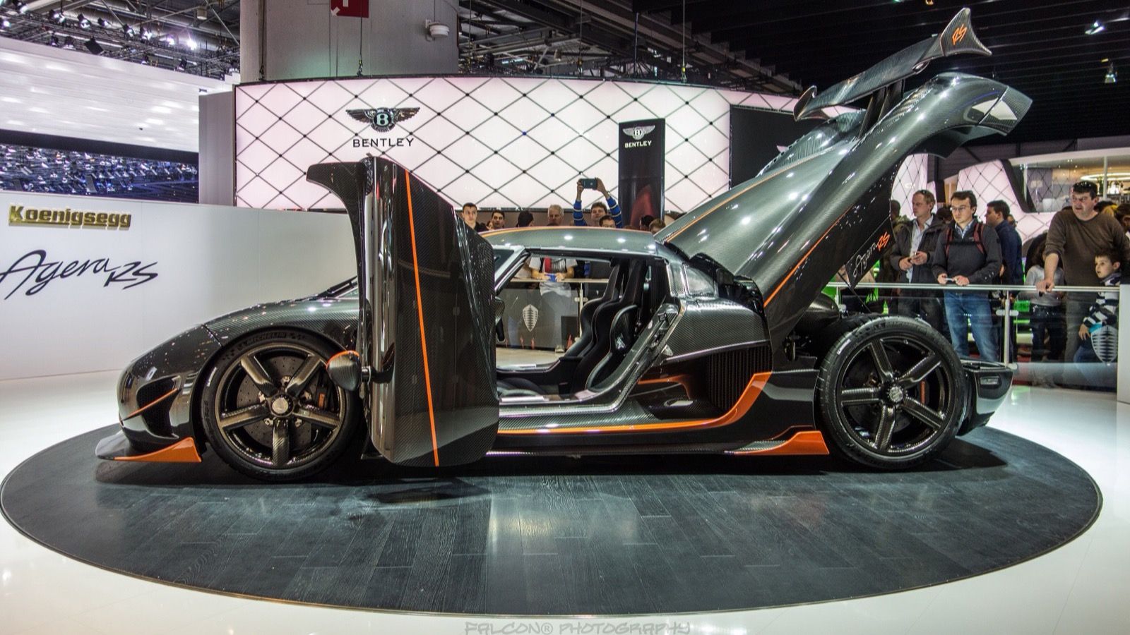 Bare carbon-fibre Koenigsegg Agera RS with orange accents on the Geneva Motor Show stand, side profile with doors raised