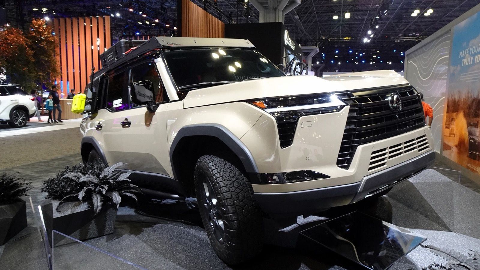 Sand-coloured 2024 Lexus GX 550 Overtrail on an auto-show stand, front three-quarter view