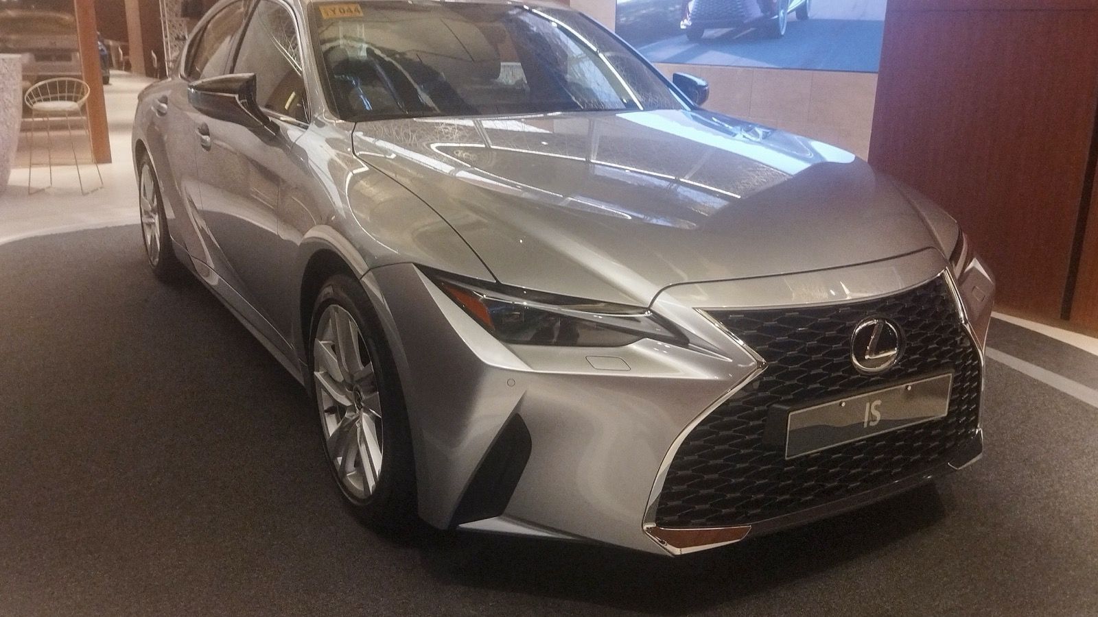 Silver 2023 Lexus IS 300h on an indoor display stand, front three-quarter view