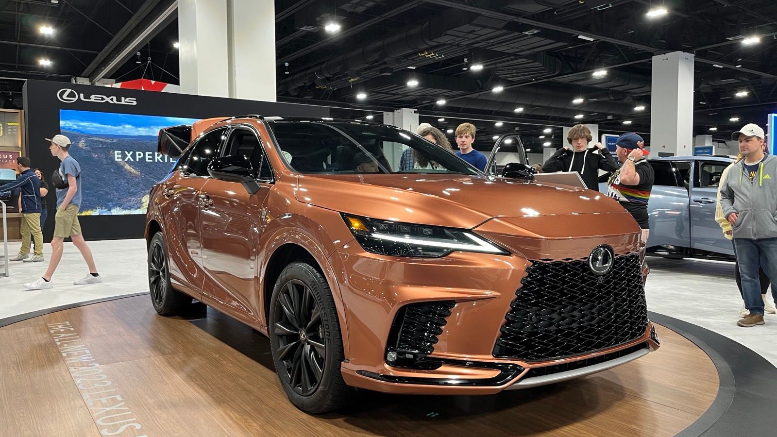Copper-orange fifth-generation Lexus RX on an auto-show turntable, front three-quarter view