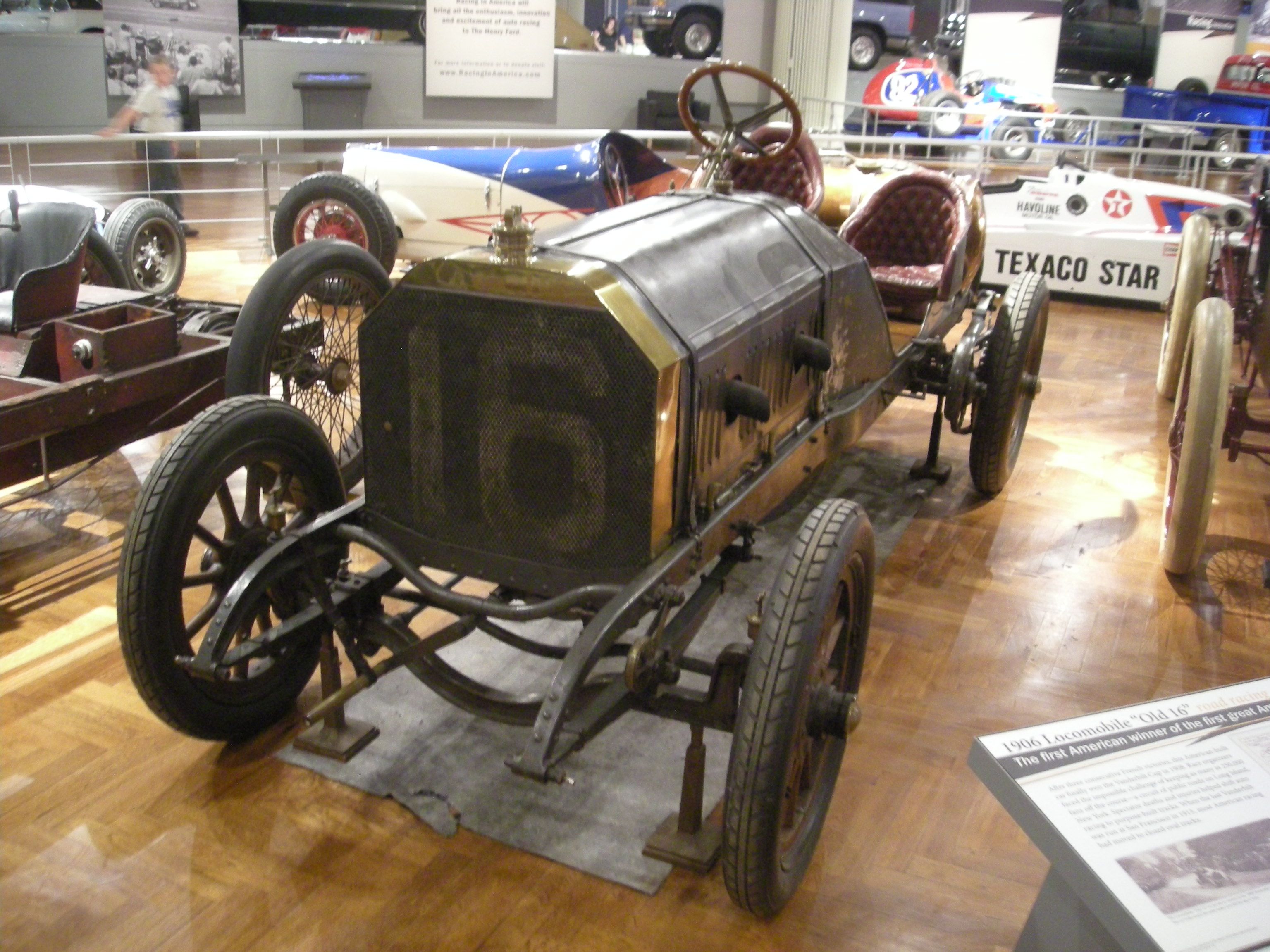 Locomobile 'Old 16' race car with number 16 grille on museum display, front three-quarter view