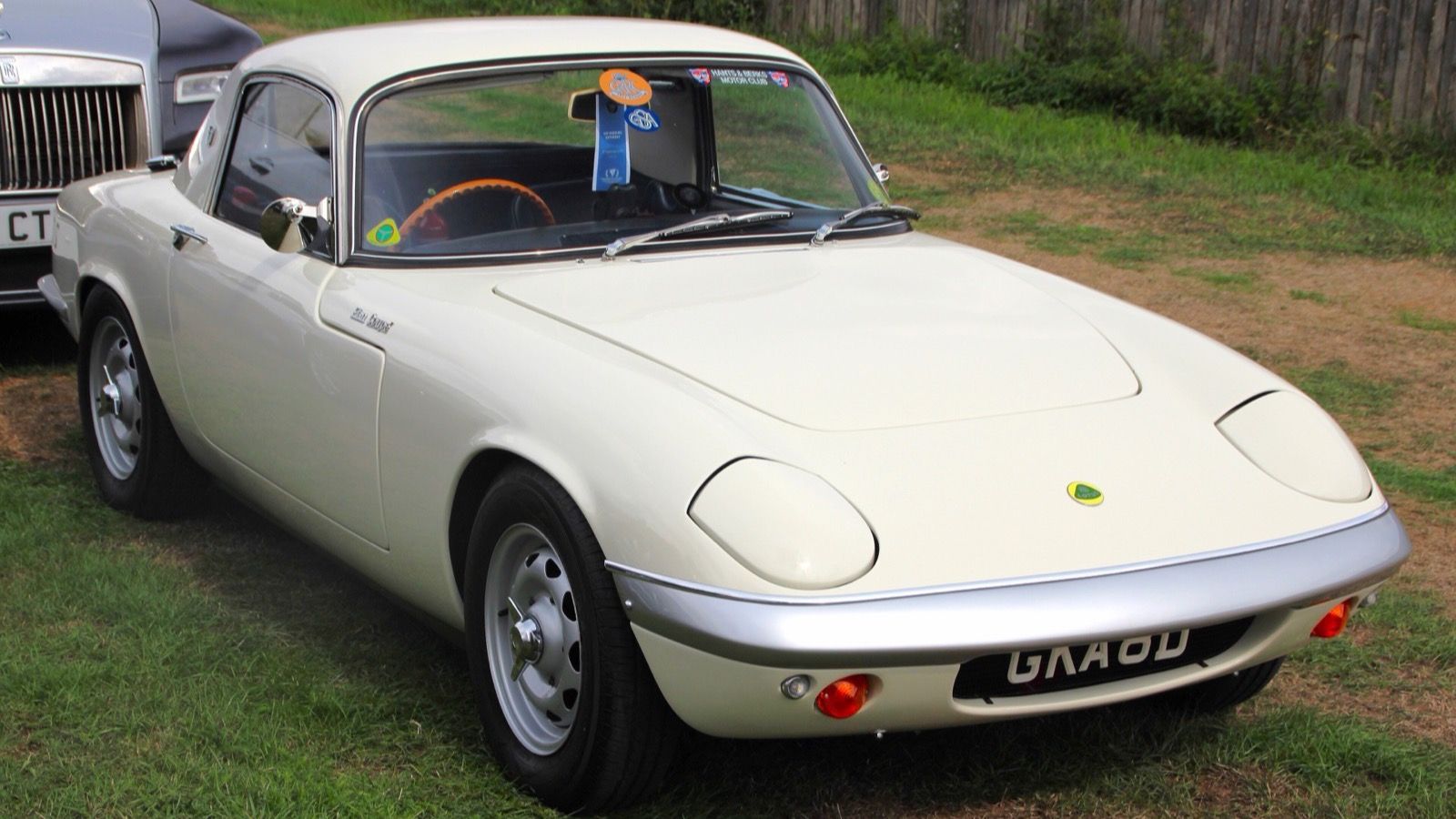 White 1966 Lotus Elan fixed-head coupe on grass, front three-quarter view.