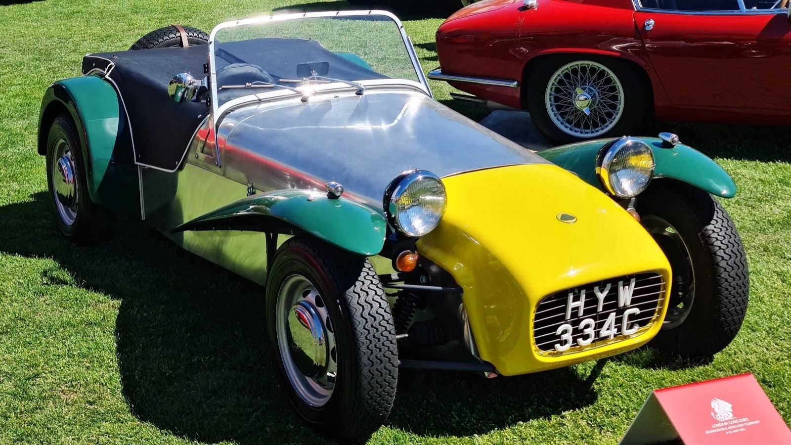 Green, yellow and aluminium 1965 Lotus Seven S2 on grass, front three-quarter view.