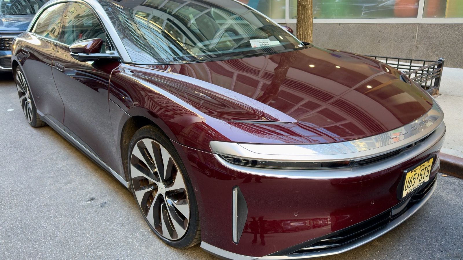 Dark red Lucid Air sedan parked on a city street, front three-quarter view