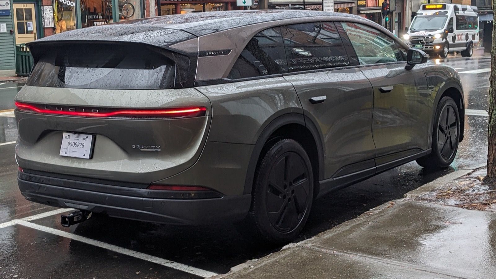 Green 2026 Lucid Gravity SUV parked on a wet town street, rear three-quarter view
