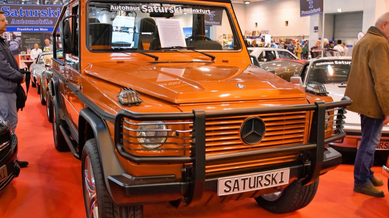 Orange 1995 Puch G-Klasse W463 230 GE cabriolet on a show stand, front three-quarter view