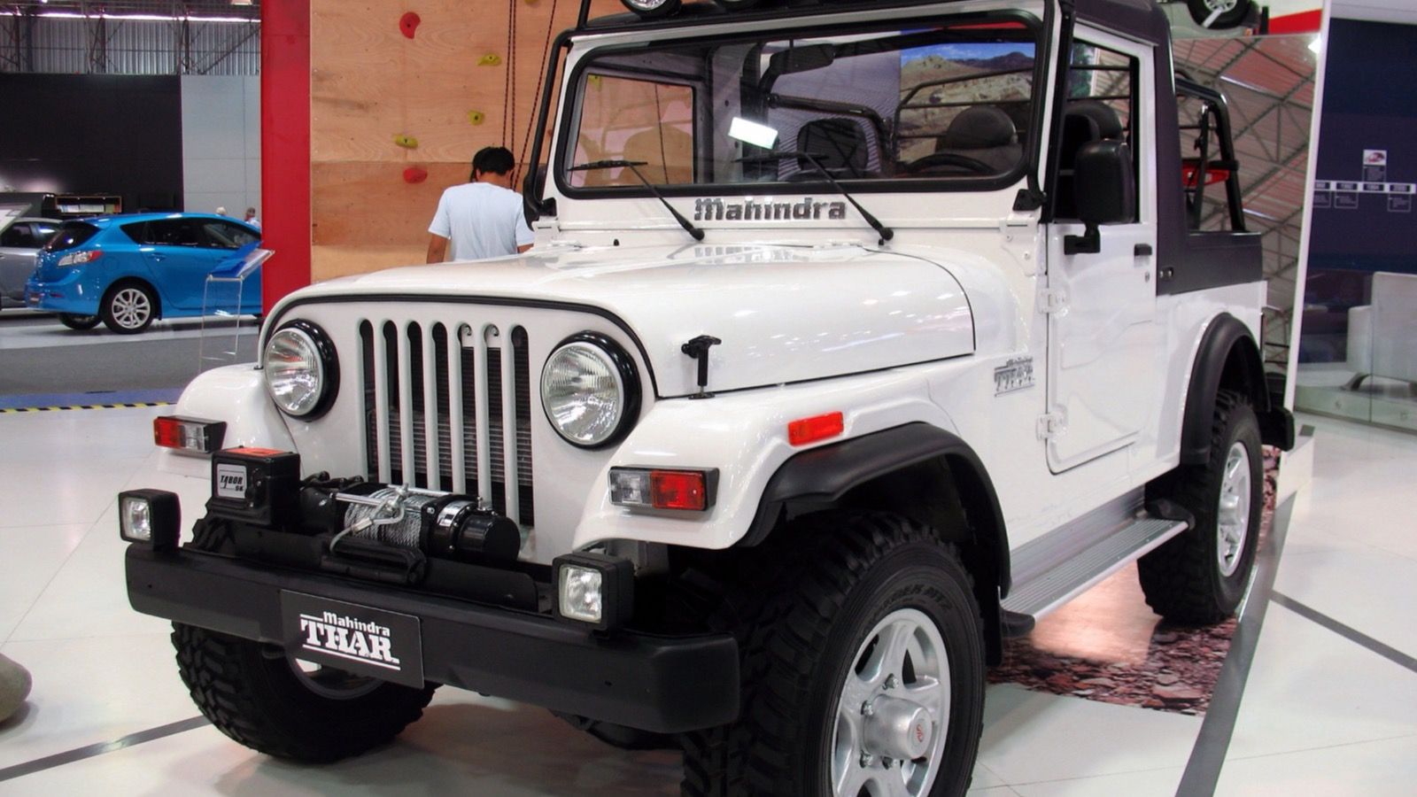 White 2011 Mahindra Thar with roof-mounted spotlights on an auto-show stand, front three-quarter view