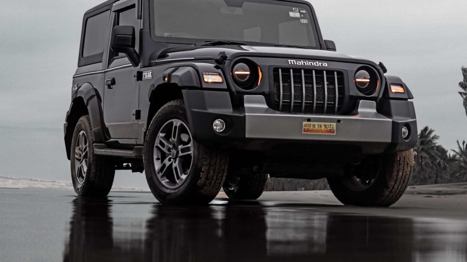 Grey second-generation Mahindra Thar hard-top parked on a wet beach, front three-quarter view