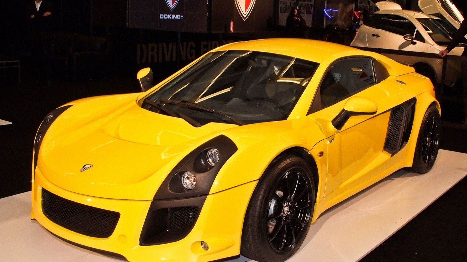 Yellow Mastretta MXT coupé on a motor show stand, front three-quarter view