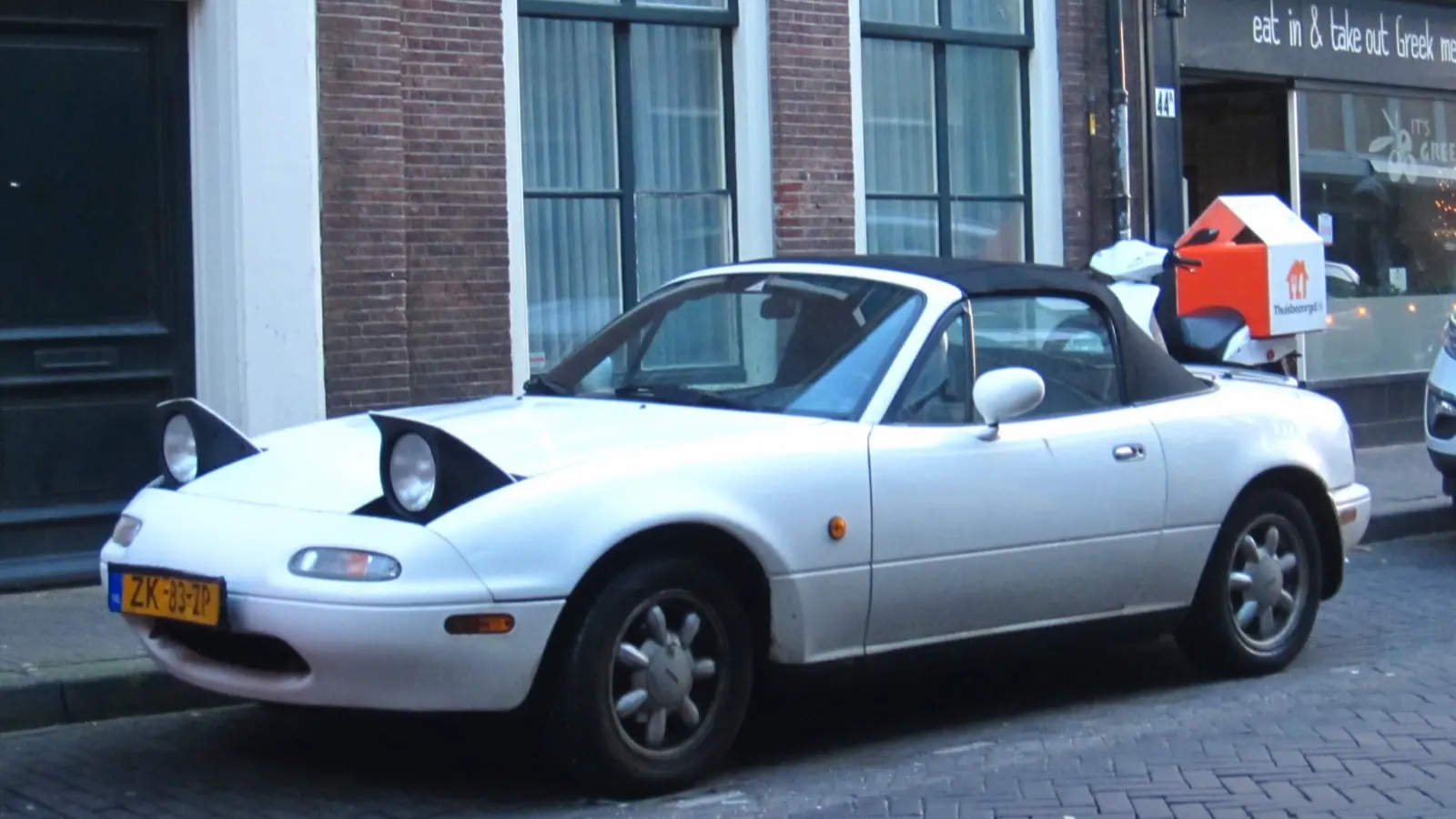 First-generation Mazda MX-5 Miata (NA) — white convertible with pop-up headlights raised, front three-quarter view
