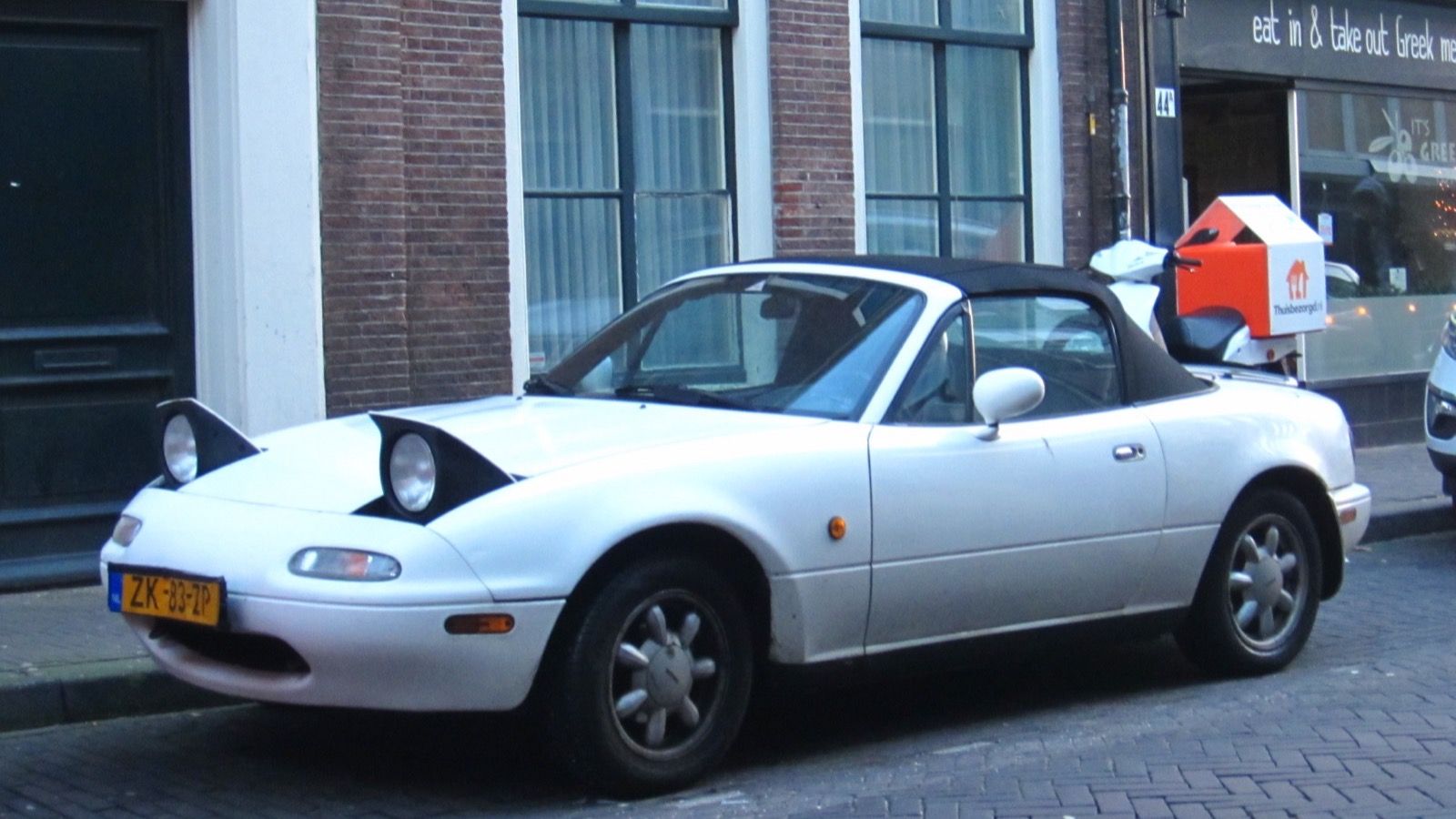 First-generation Mazda MX-5 Miata (NA) — white convertible with pop-up headlights raised, front three-quarter view