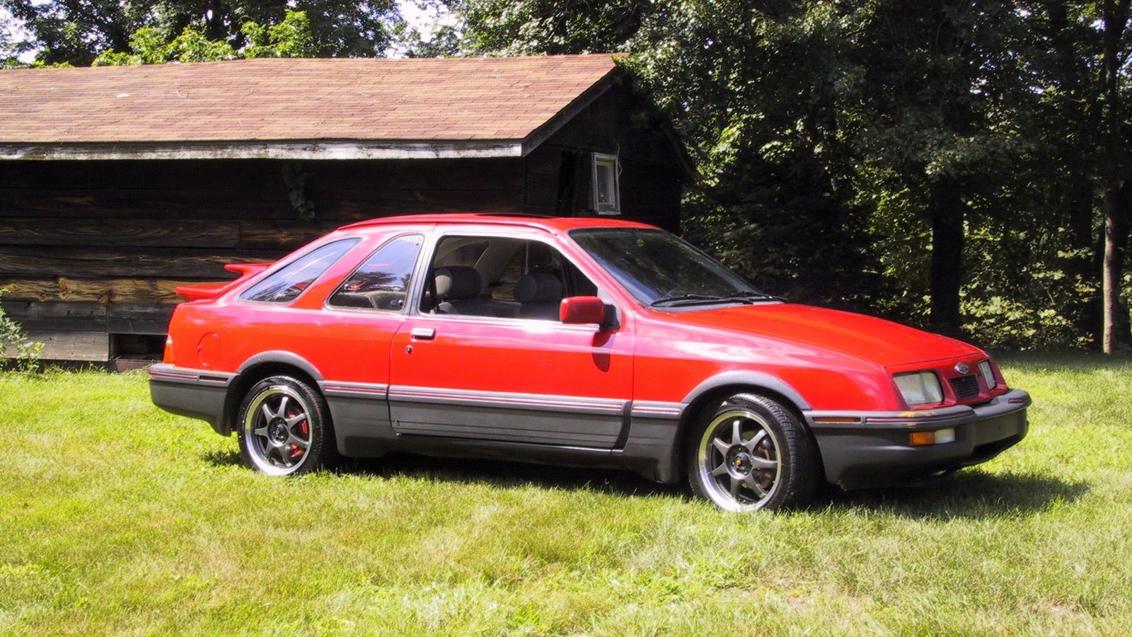 Red 1985 Merkur XR4Ti in side profile, showing the twin-wing rear spoiler and two-tone lower body cladding