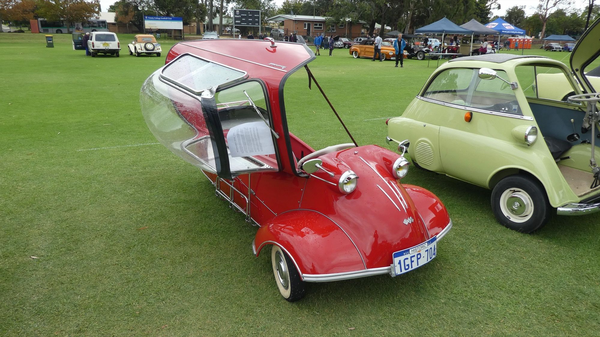 Red 1961 Messerschmitt KR200 with its bubble canopy hinged open at a classic car show, front three-quarter view