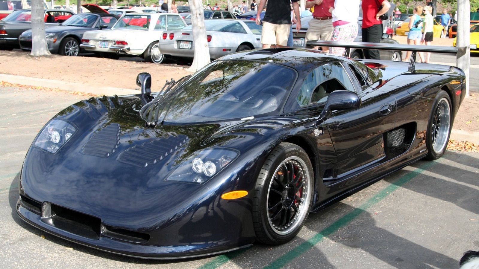 Dark blue Mosler MT900S with rear wing parked at a car meet, front three-quarter view