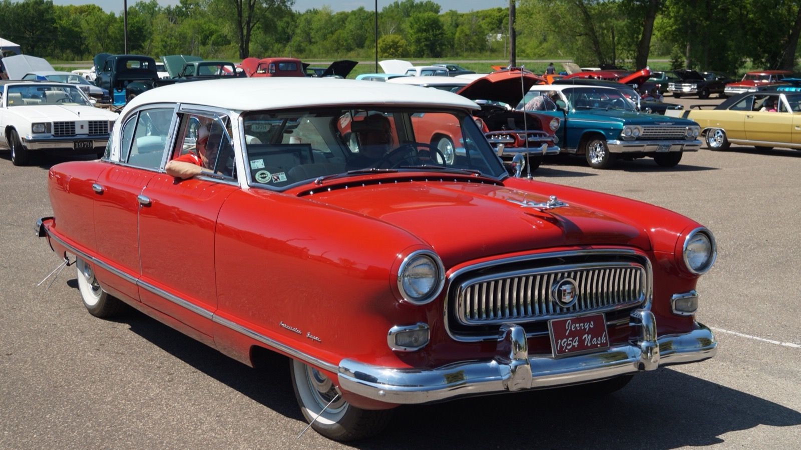 Red 1954 Nash Ambassador Super four-door sedan with white roof, front three-quarter view in a car show parking lot